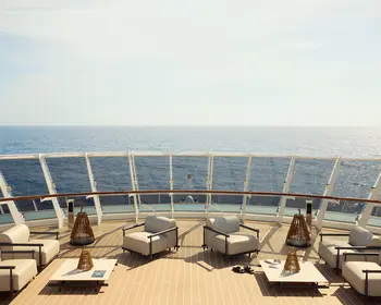 Zu sehen ist die Aussicht von einem Kreuzfahrtschiff auf das offene Meer. An Deck sind Lounge-Möbel platziert.