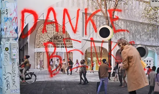 Rote Graffiti-Schrift Danke Benko an einer verhängten Fassade einer Baustelle, davor gehen Passanten vorbei.
