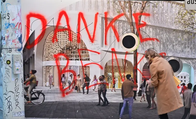 Rote Graffiti-Schrift Danke Benko an einer verhängten Fassade einer Baustelle, davor gehen Passanten vorbei.