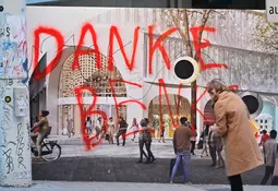 Rote Graffiti-Schrift Danke Benko an einer verhängten Fassade einer Baustelle, davor gehen Passanten vorbei.