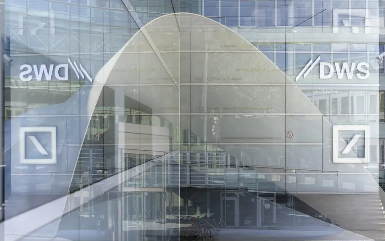 Das DWS-Logo ist auf einer Glasscheibe einer modernen Bürofassade in Frankfurt am Main zu sehen, im Hintergrund spiegeln sich weitere Gebäudeteile.