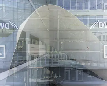 Das DWS-Logo ist auf einer Glasscheibe einer modernen Bürofassade in Frankfurt am Main zu sehen, im Hintergrund spiegeln sich weitere Gebäudeteile.