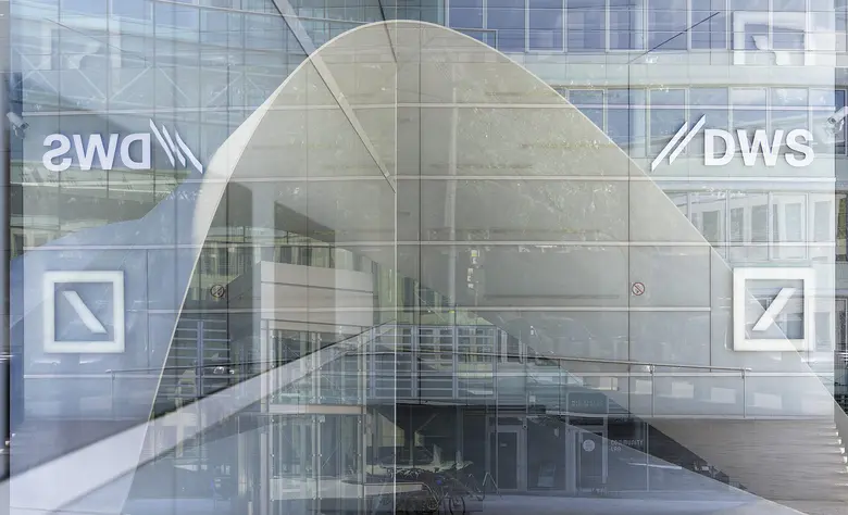 Das DWS-Logo ist auf einer Glasscheibe einer modernen Bürofassade in Frankfurt am Main zu sehen, im Hintergrund spiegeln sich weitere Gebäudeteile.
