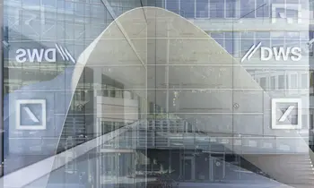 Das DWS-Logo ist auf einer Glasscheibe einer modernen Bürofassade in Frankfurt am Main zu sehen, im Hintergrund spiegeln sich weitere Gebäudeteile.