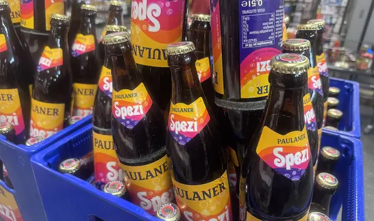Mehrere Paulaner Spezi Flaschen in einem blauen Getränkekasten, die Etiketten mit dem orangefarbenen Paulaner Spezi Logo gut sichtbar.