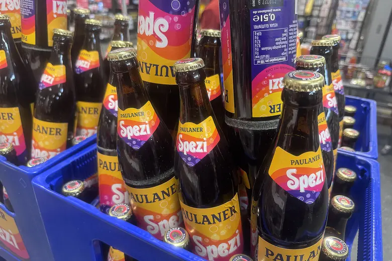 Mehrere Paulaner Spezi Flaschen in einem blauen Getränkekasten, die Etiketten mit dem orangefarbenen Paulaner Spezi Logo gut sichtbar.