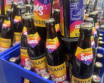 Mehrere Paulaner Spezi Flaschen in einem blauen Getränkekasten, die Etiketten mit dem orangefarbenen Paulaner Spezi Logo gut sichtbar.