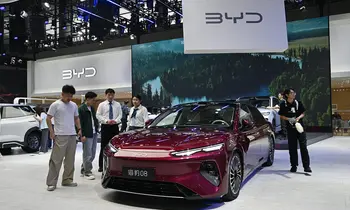 Weinrote Limousine auf einem Messestand, davor mehrere Besucher, darüber ein großes Banner mit dem BYD-Logo.