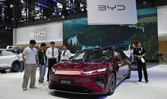 Weinrote Limousine auf einem Messestand, davor mehrere Besucher, darüber ein großes Banner mit dem BYD-Logo.