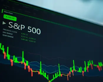 Computermonitor mit S&P-500-Kursanzeige, Candlestick-Chart in Grün und Rot sowie Kursdaten auf dunklem Hintergrund.