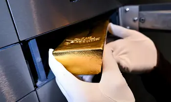 Eine behandschuhte Hand legt einen glänzenden Goldbarren in ein offenes Schließfach aus Metall.