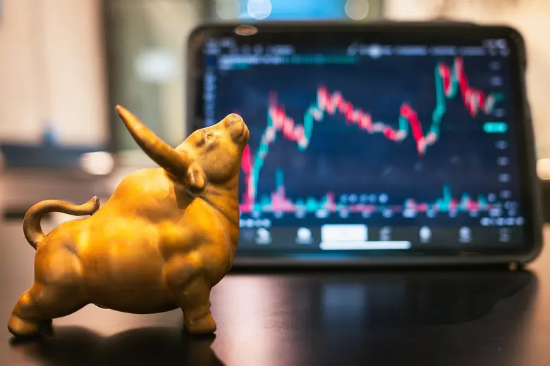 Goldene Bullenfigur steht vor einem Bildschirm mit einem Aktienchart.