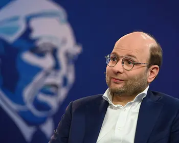 Bastian Nominacher sitzt mit Mikrofon auf einer Bühne.