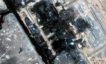 Satellitenaufnahme einer großen Industrieanlage in der Wüste, bei der mehrere Gebäudekomplexe durch Feuer schwarz verkohlt und teilweise zerstört sind.