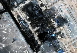 Satellitenaufnahme einer großen Industrieanlage in der Wüste, bei der mehrere Gebäudekomplexe durch Feuer schwarz verkohlt und teilweise zerstört sind.