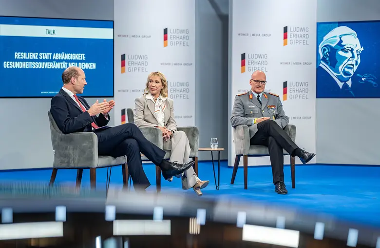 Drei Personen sitzen bei einer Podiumsdiskussion auf einer Bühne des Ludwig-Erhard-Gipfels.