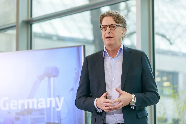 Mann im Anzug mit Brille und Headset vor einem Bildschirm.
