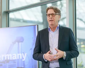 Mann im Anzug mit Brille und Headset vor einem Bildschirm.
