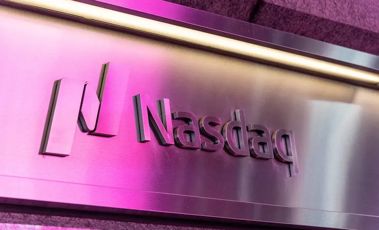 Metallschild mit dem Nasdaq-Logo und dem Schriftzug Nasdaq, das in Pink und Magenta beleuchtet wird.