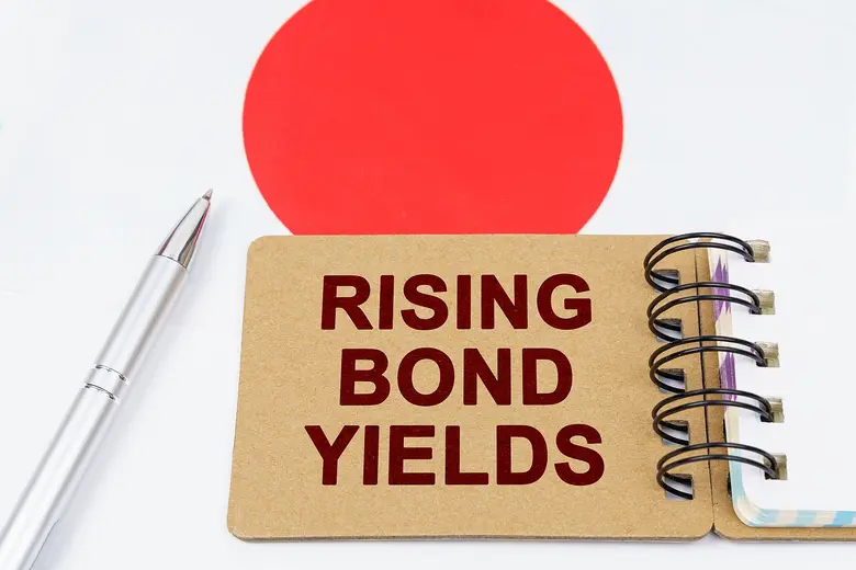 Notizkarte mit der Aufschrift „Rising Bond Yields“ vor Japans Nationalflagge – Symbol für steigende Anleiherenditen und Zinsrisiken.