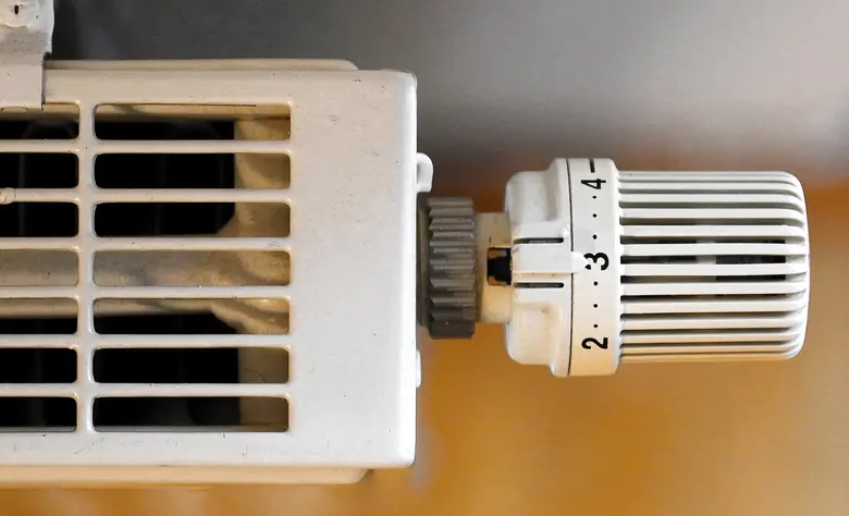 Nahaufnahme eines Thermostatventils an einem weißen Heizkörper mit Lüftungsschlitzen.