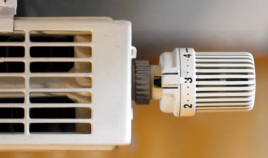 Nahaufnahme eines Thermostatventils an einem weißen Heizkörper mit Lüftungsschlitzen.