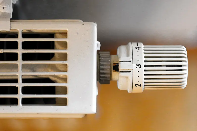 Nahaufnahme eines Thermostatventils an einem weißen Heizkörper mit Lüftungsschlitzen.