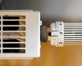 Nahaufnahme eines Thermostatventils an einem weißen Heizkörper mit Lüftungsschlitzen.