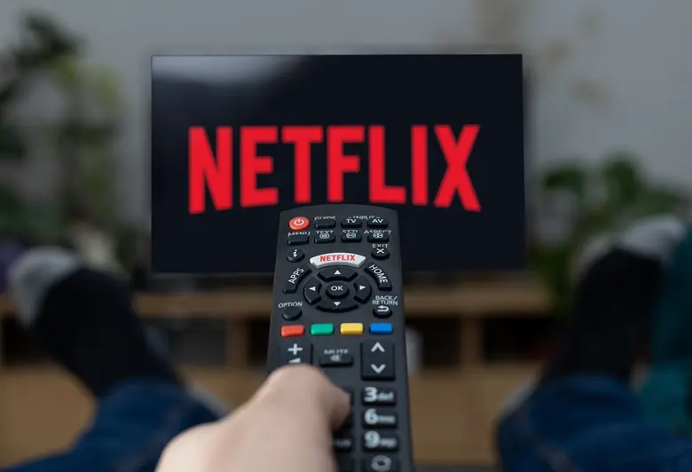 Eine Hand hält eine Fernbedienung, die auf einen Fernseher mit dem Netflix-Logo gerichtet ist.