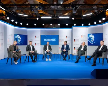 Sechs Männer sitzen bei einer Podiumsdiskussion auf einer blau beleuchteten Bühne.