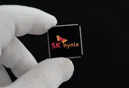 Zwei Finger in weißen Handschuhen halten einen schwarzen Chip mit dem Logo von SK hynix vor schwarzem Hintergrund.