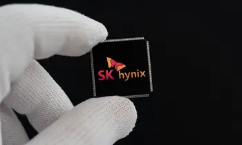 Zwei Finger in weißen Handschuhen halten einen schwarzen Chip mit dem Logo von SK hynix vor schwarzem Hintergrund.