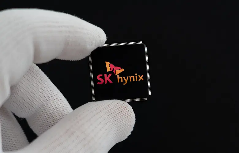 Zwei Finger in weißen Handschuhen halten einen schwarzen Chip mit dem Logo von SK hynix vor schwarzem Hintergrund.