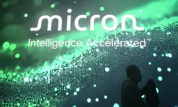 Großes beleuchtetes Micron-Logo mit dem Slogan Intelligence Accelerated auf einer Messewand, davor die Silhouette einer Person.