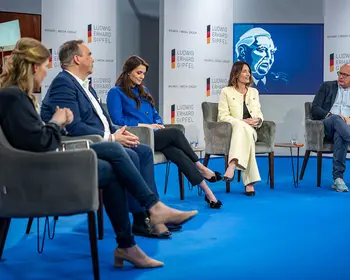 Mehrere Personen sitzen bei einer Podiumsdiskussion auf einer Bühne.