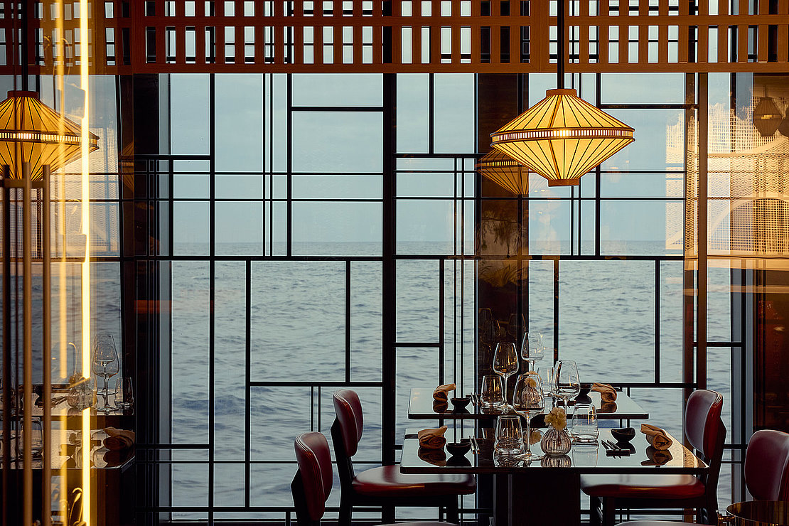 Das Foto zeigt ein Restaurant auf einem Kreuzfahrtschiff mit Blick durch die gläserne Fassade.