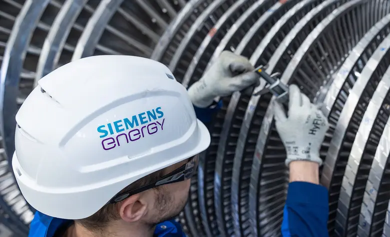 Mitarbeiter mit weißem Schutzhelm mit Siemens-Energy-Logo arbeitet mit einem Werkzeug an den Schaufeln einer großen Dampfturbine.