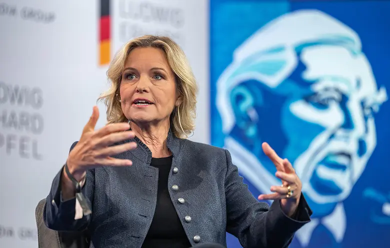 Carola Ferstl spricht bei einer Podiumsdiskussion vor blauem Hintergrund.