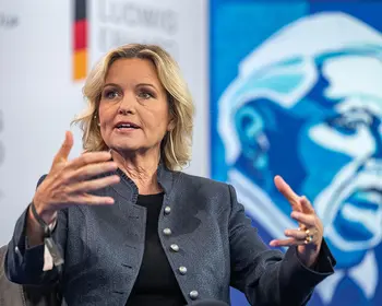 Carola Ferstl spricht bei einer Podiumsdiskussion vor blauem Hintergrund.