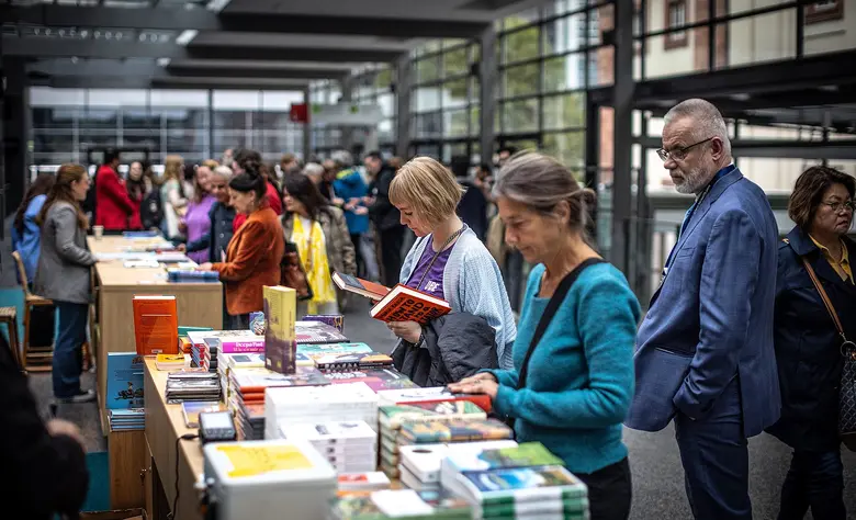 Menschen stöbern an einem Büchertisch auf der Frankfurter Buchmesse. Im modernen Messebereich blättern Besucherinnen und Besucher durch zahlreiche ausgestellte Bücher und Neuerscheinungen.