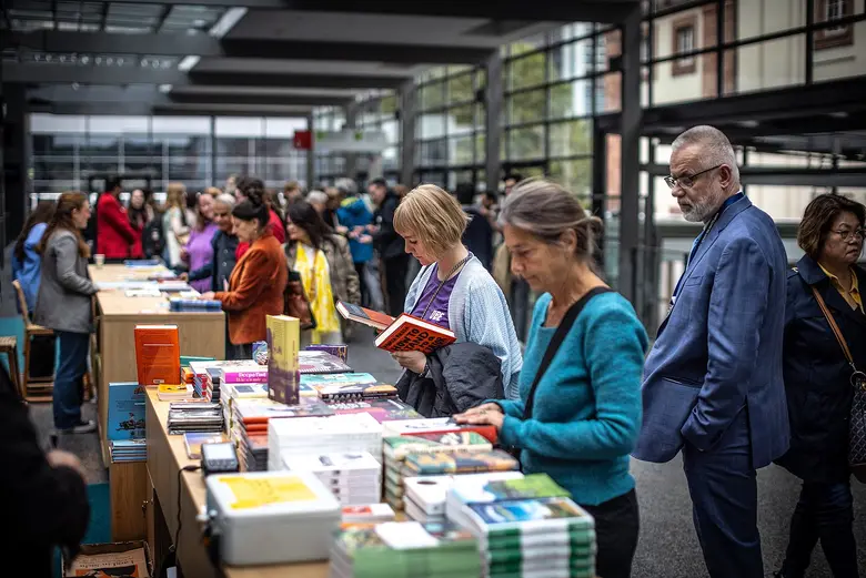 Menschen stöbern an einem Büchertisch auf der Frankfurter Buchmesse. Im modernen Messebereich blättern Besucherinnen und Besucher durch zahlreiche ausgestellte Bücher und Neuerscheinungen.