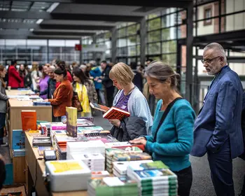 Menschen stöbern an einem Büchertisch auf der Frankfurter Buchmesse. Im modernen Messebereich blättern Besucherinnen und Besucher durch zahlreiche ausgestellte Bücher und Neuerscheinungen.