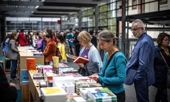 Menschen stöbern an einem Büchertisch auf der Frankfurter Buchmesse. Im modernen Messebereich blättern Besucherinnen und Besucher durch zahlreiche ausgestellte Bücher und Neuerscheinungen.