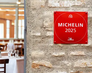 Rotes MICHELIN-2025-Schild an einer Steinwand neben einem Restaurantbereich.
