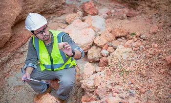 Geologe mit Helm und Warnweste untersucht Gestein in felsigem Gelände.