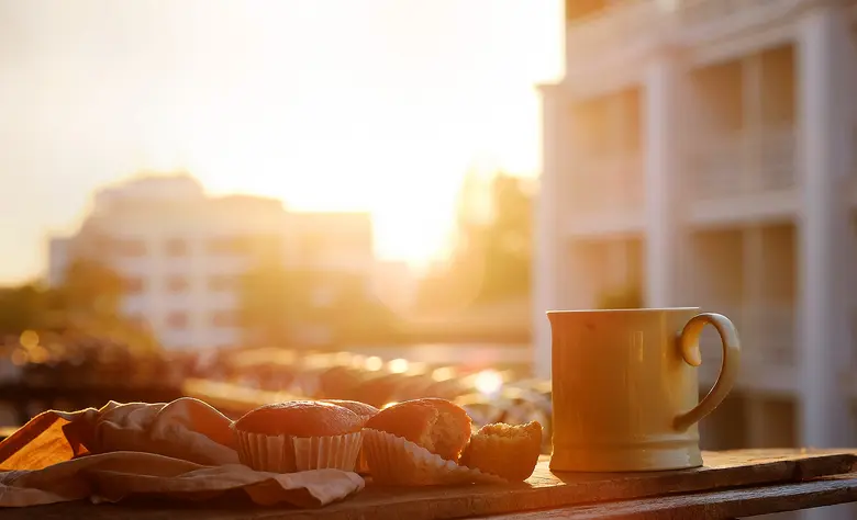 Muffins und eine Tasse Kaffee stehen auf einem Balkon bei Sonnenaufgang in der Stadt