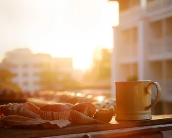 Muffins und eine Tasse Kaffee stehen auf einem Balkon bei Sonnenaufgang in der Stadt