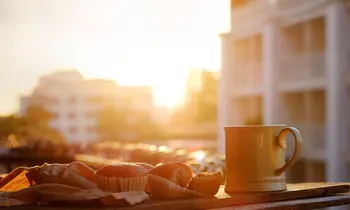 Muffins und eine Tasse Kaffee stehen auf einem Balkon bei Sonnenaufgang in der Stadt