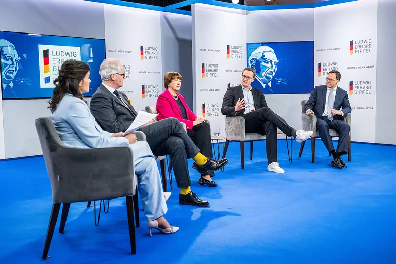 Fünf Personen sitzen bei einer Podiumsdiskussion auf einer Bühne mit Ludwig-Erhard-Gipfel-Logos.