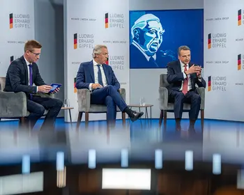Drei Männer sitzen bei einer Podiumsdiskussion auf einer Bühne mit Ludwig-Erhard-Gipfel-Logos.